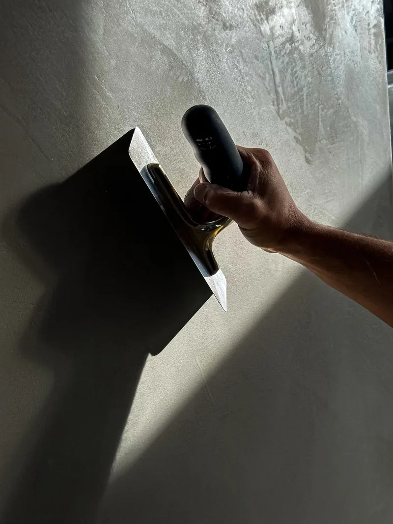 A hand trowel applying wet plaster to a wall