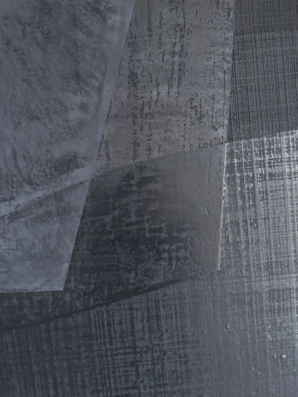 Macro detail of mottled charcoal-gray textured surface with a smoother triangular gray facet at center.