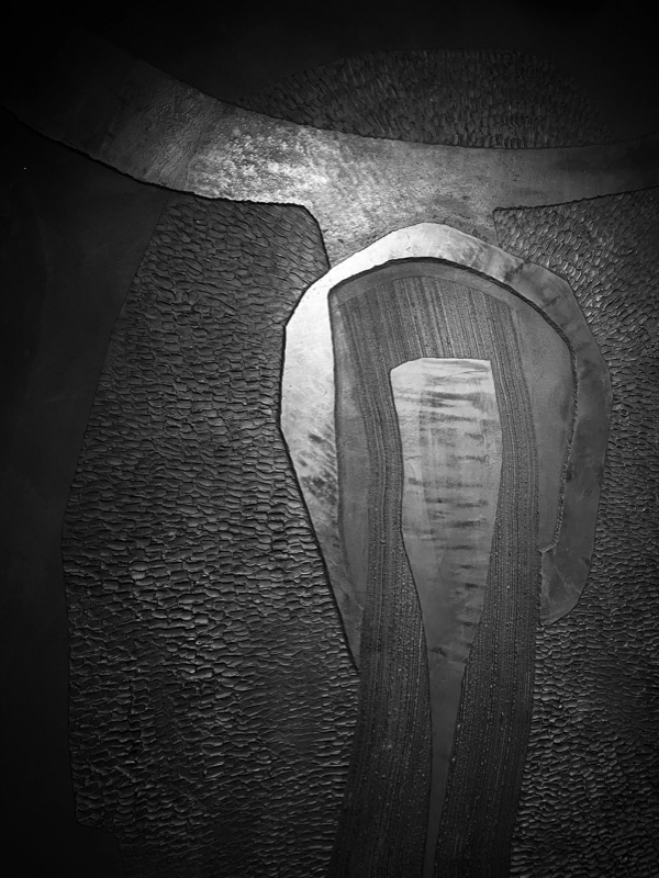 Close view of a bull-mask relief's upper section, horns and central pale arch glowing against black pebbled shoulders.
