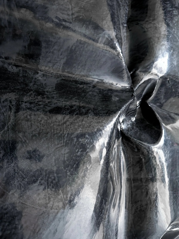 Extreme close-up of the folded, draped surface, resembling crumpled metallic fabric with deep creases and strong light.