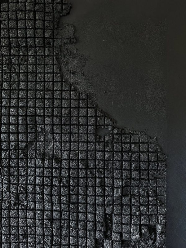 Portrait panel of black grid and waffle relief meeting a smooth black field.