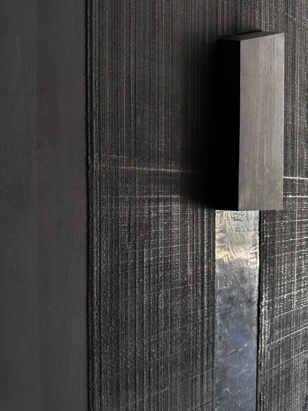 Close-up of an angular wedge element with its dramatic cast shadow against the combed black textured panel.