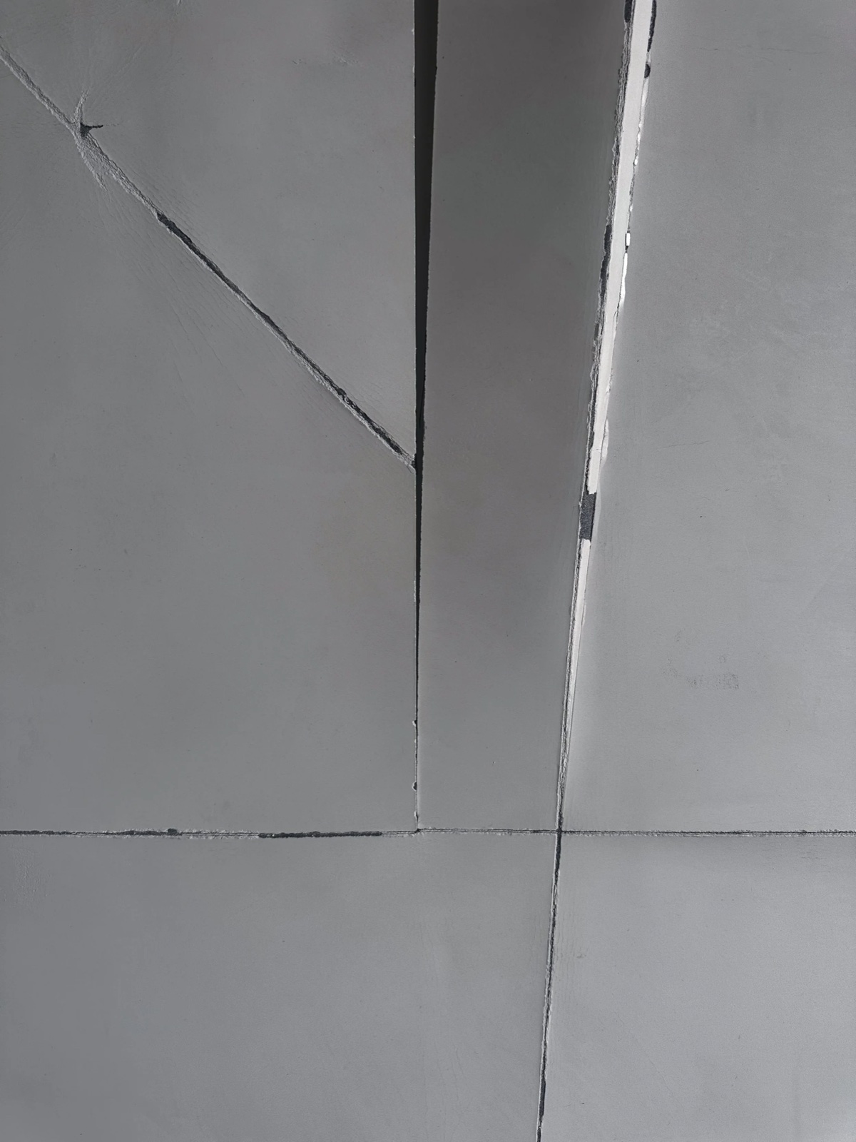 Pale relief panel with radiating crack lines beside a smooth diagonal folded section, casting a real shadow.