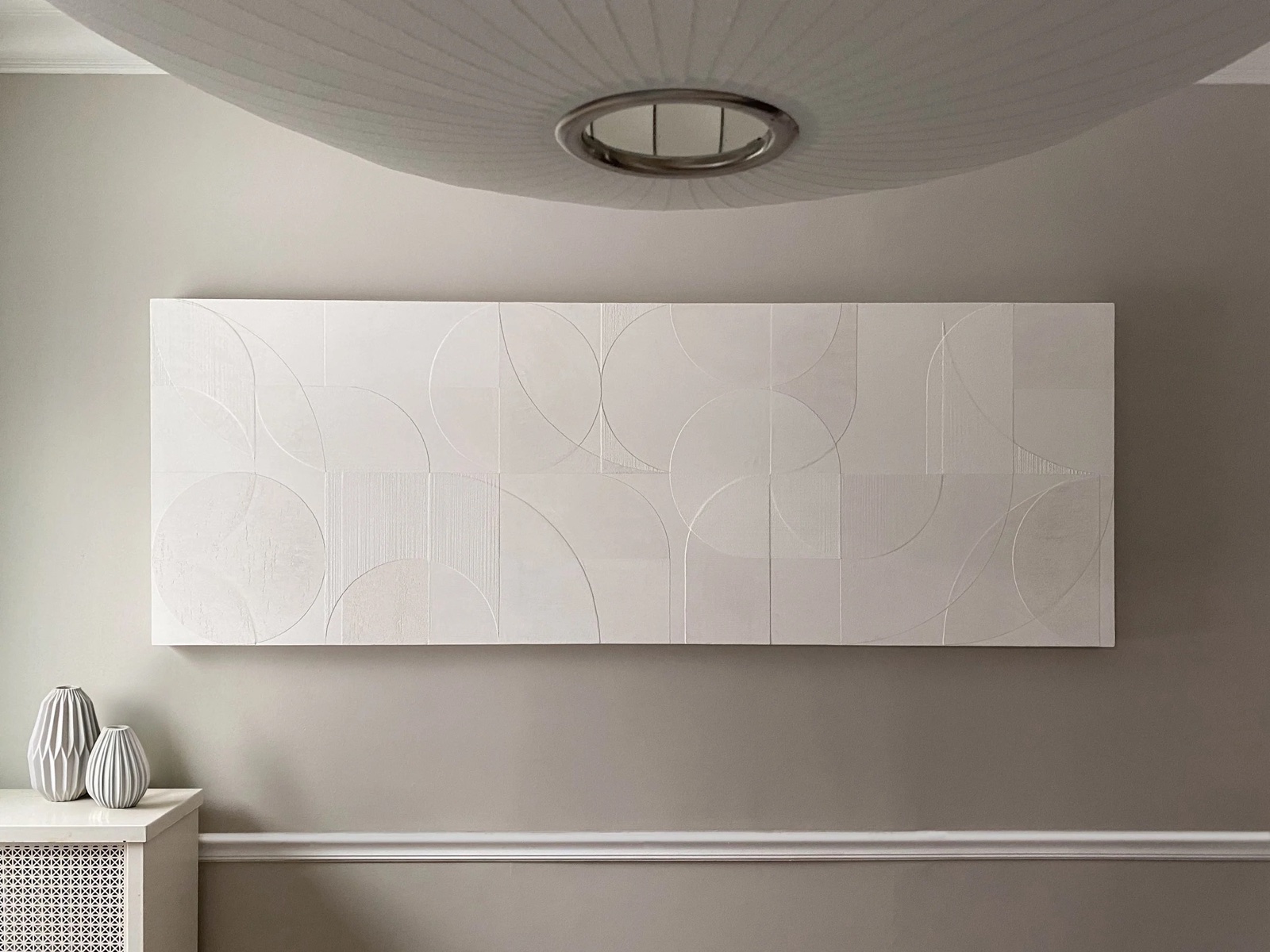 A wide geometric plaster arc panel above a console in a residential room.