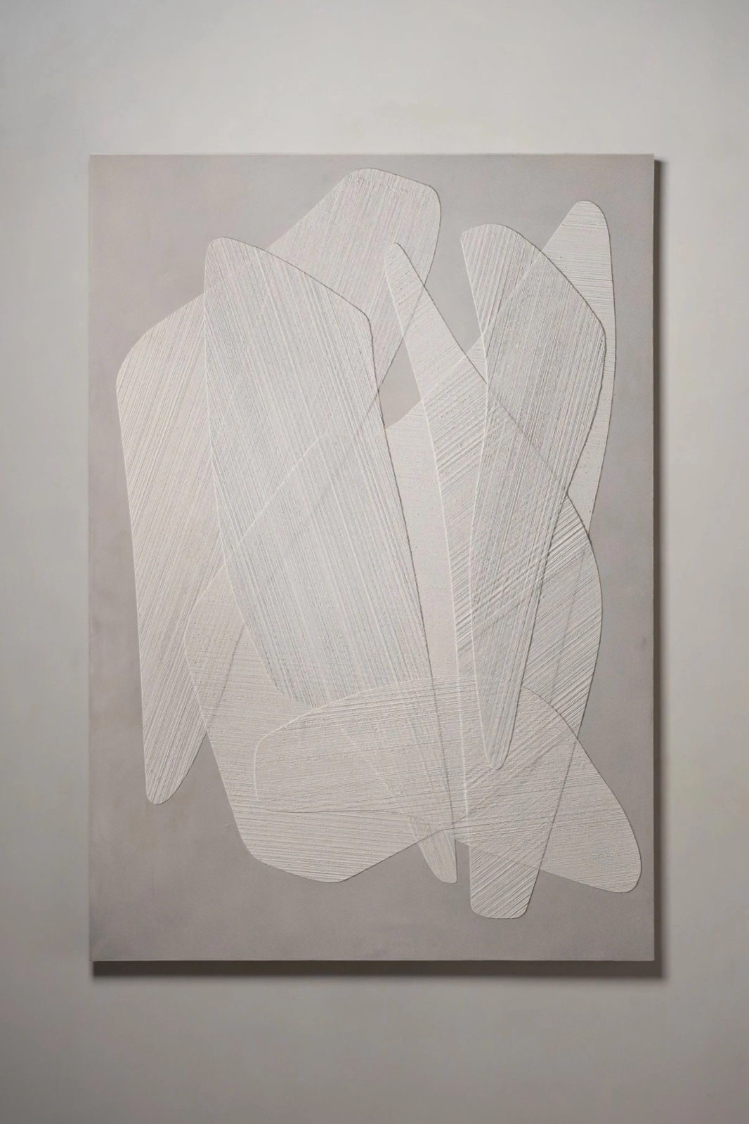 A bone white combed plaster panel of overlapping angular forms on a gallery wall.