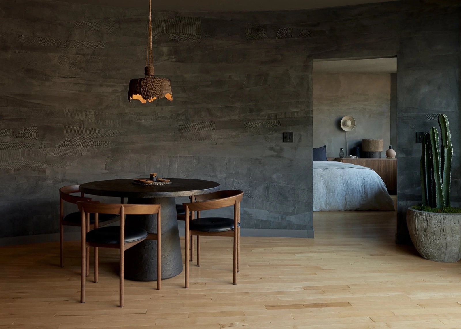 A curved charcoal limewash wall wrapping a dining and bedroom suite with walnut furniture.
