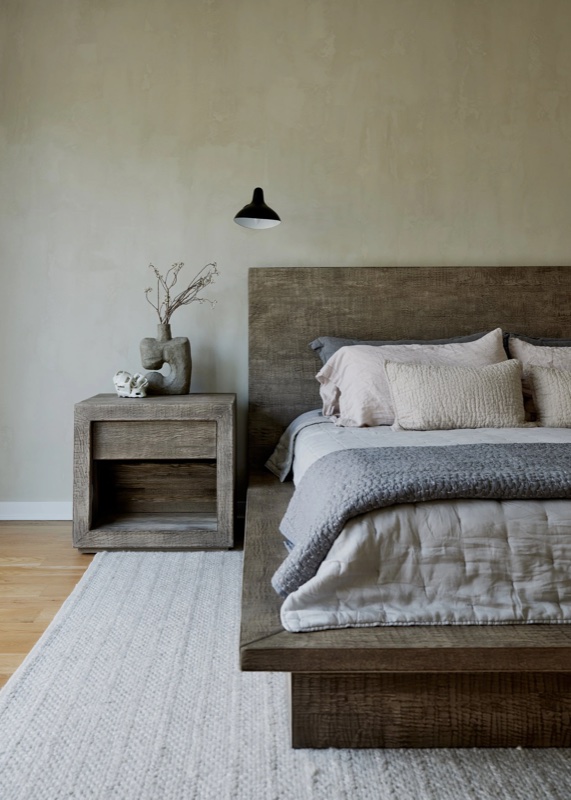 Bedroom scene with a dark wood platform bed and layered gray linens against a cloudy plaster accent wall.