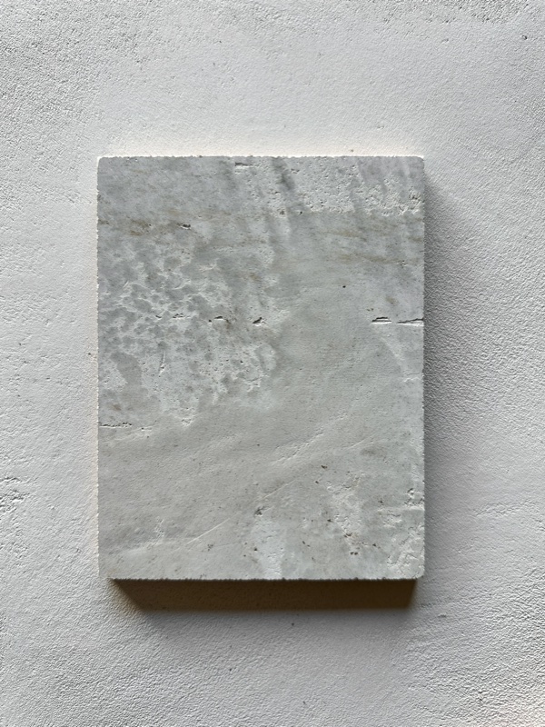 A rectangular finish sample mounted on an off-white textured wall, showing a matte stone-gray surface.