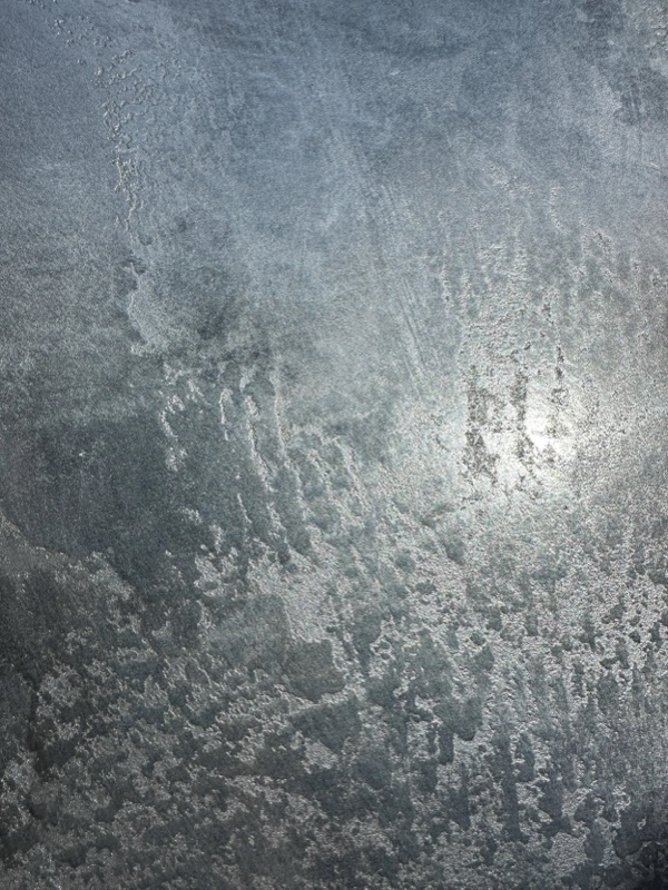 Full-frame macro of a steel-blue metallic finish with mottled passages and a bright reflective glare.