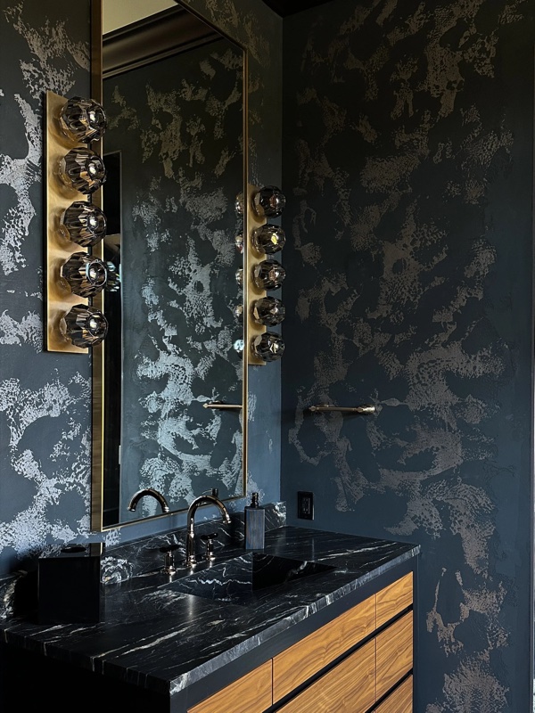 A dark bathroom vanity with mottled silver-on-black plaster walls around a tall mirror.