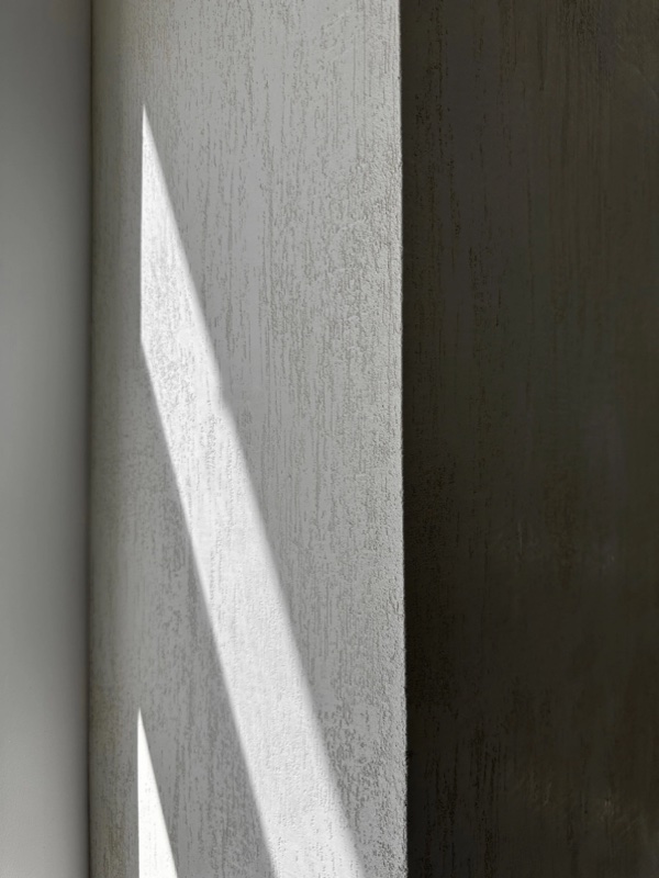 A corner where a diagonal shaft of daylight crosses a plaster wall, meeting a darker plaster wall at a sharp vertical.