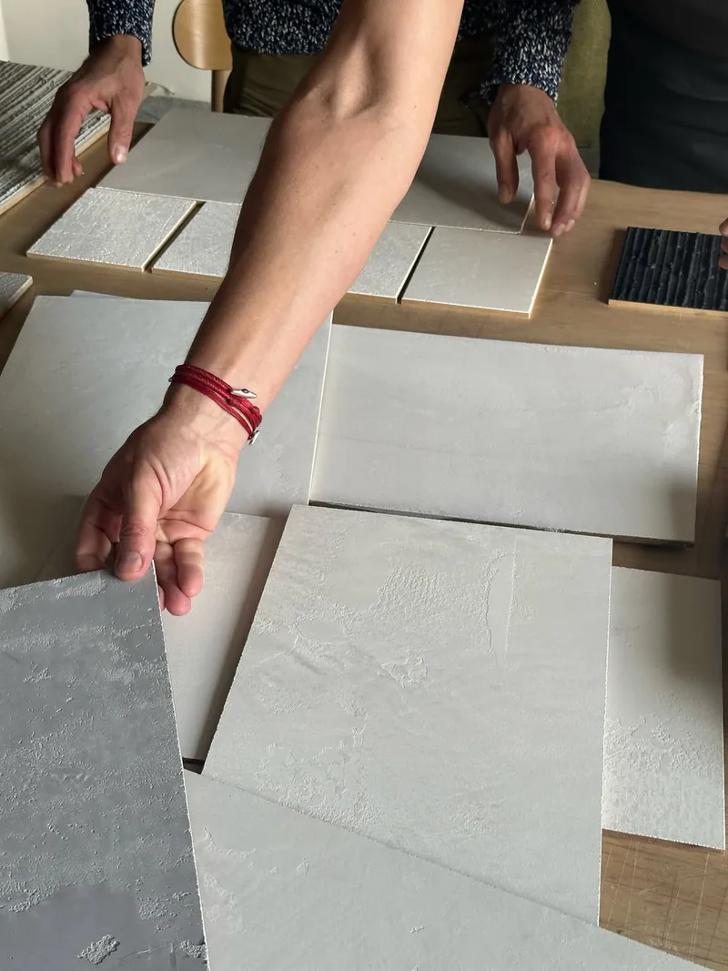 Hands arranging custom plaster sample swatches on the studio table