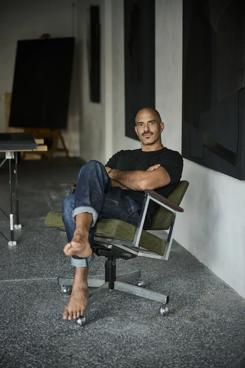 Peter Varga seated in the studio, dark relief panels behind him