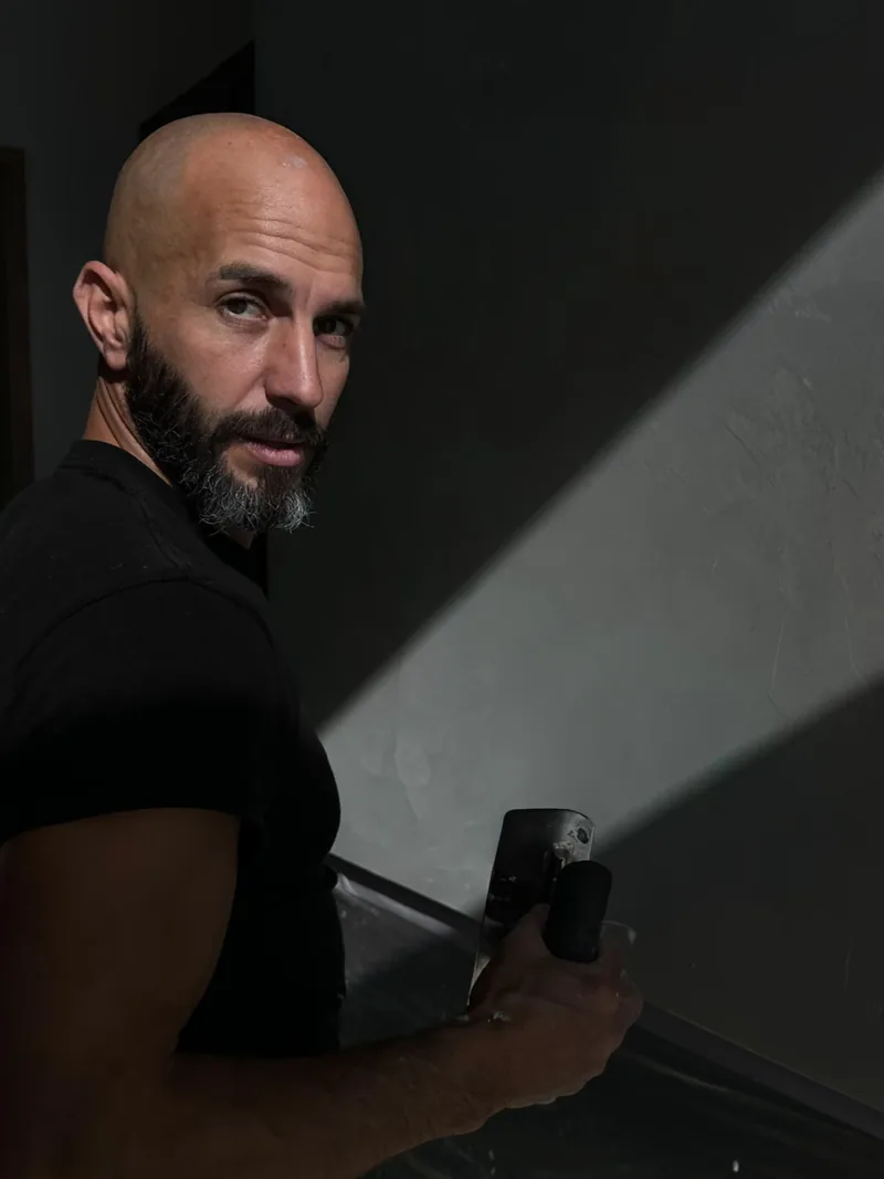 Robert Varga at the wall, trowel in hand, raking light across fresh plaster
